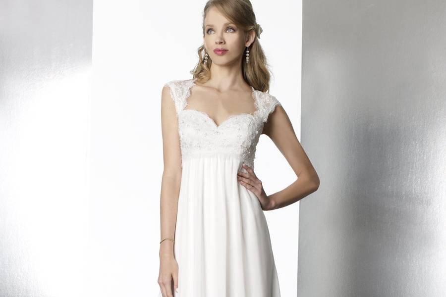 Style T569An A-line baby doll chiffon gown featuring lace detailing across the bodice and cap sleeves. The cap sleeves transition into a keyhole back. Subtle beading accents the bodice.