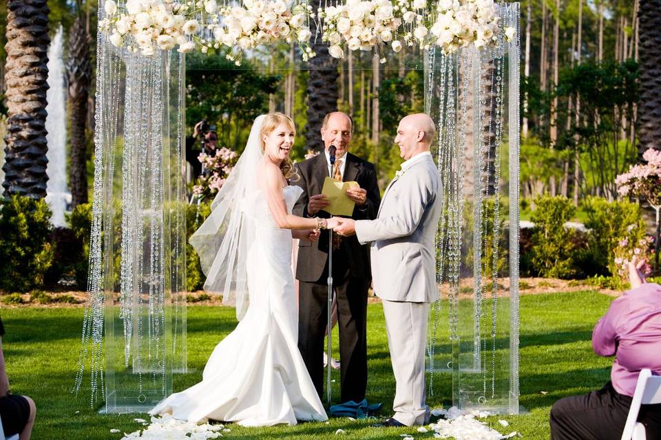 Lucite arbor embellished with crystal strands and a band of david austin garden roses complimented with orchid blossoms. Ceremony on the lawn at cross water hall at nocatee, ponte vedra florida