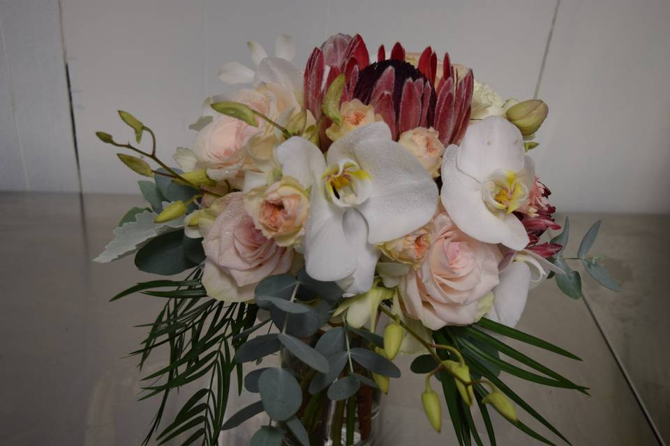 A hand tied tropical and spring mix with protea, phaleanopsis orchids and roses