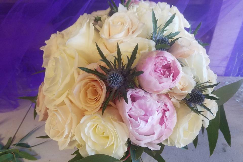 Hand tied bouquet designed with roses, peonies and accents of thistle