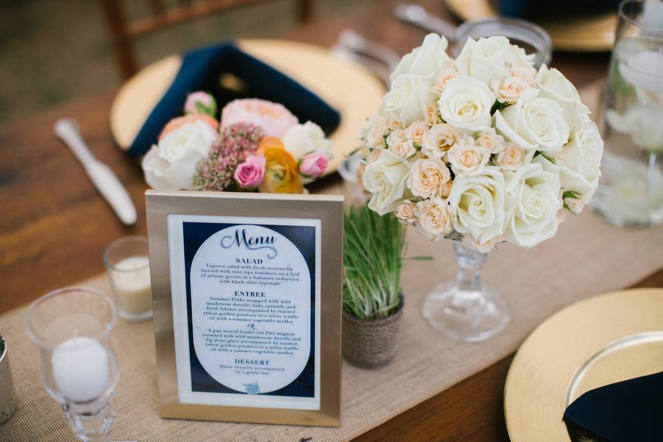 Subtle tones of creams, peaches and pinks create this tablescape centerpiece design on long wooden tables with burlap runners.