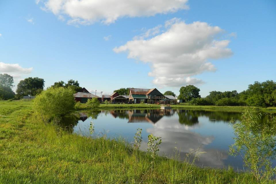 Looking north from the south side of the ranch pond. At the left is the West Work Barn, then the Corn Crib with the new Pond Pavilion on its south side, then the Wedding Barn/Events Center. To the far right and in the distance is the Indoor Arena. Note the dock on the north edge of the pond at Westwoods' Civil War Ranch.