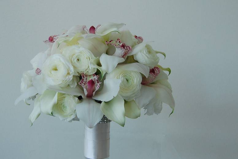 Simply elegant white bouquet with a kiss of blush pink. Cybidium orchids, ivory mini callas and lush white ranunculus arranged in a bouquet holder. Bouquet can stand upright on it's own and flowers have a moisture reservoir which assures the pristine look and freshness of your bridal bouquet.