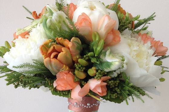 A bouquet of peonies, parrot tulips and freesia arranged in a bouquet holder.