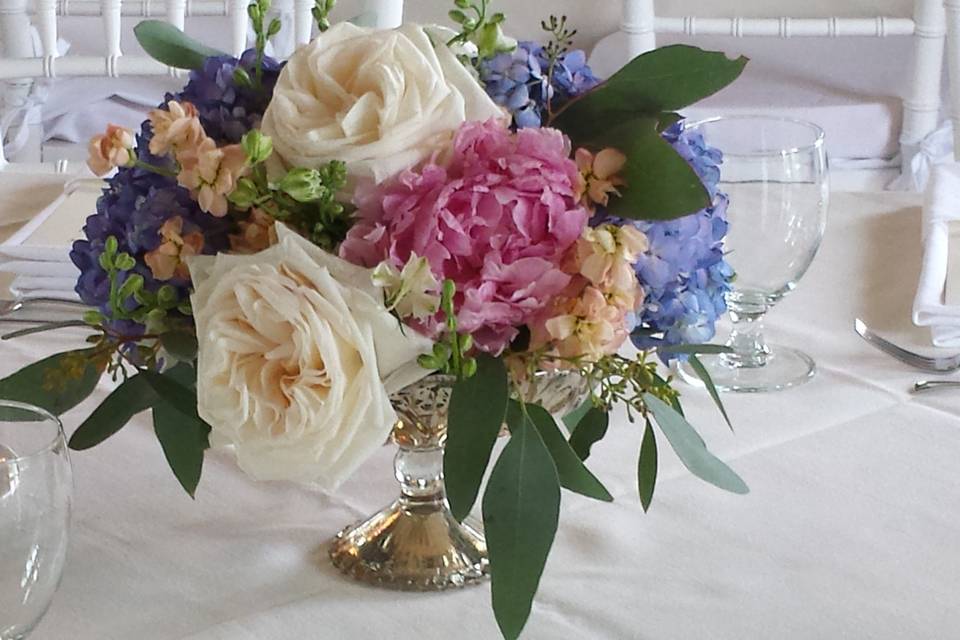 Gold compote vase dressed with hydrangeas, stock, garden roses and budding eucalyptus.