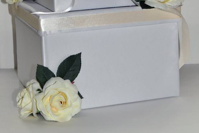 This beautiful 3-tier square wedding money box comes adorned with white satin fabric and white roses surrounding the edges.  There is a cream color satin trim along the tops of the boxes that could be customized to match your bridesmaid dresses or wedding theme colors.
The slit on the opening on the middle tier features crystal AB rhinestones along all the edges.  The top box is actually removable and can be kept as a keepsake.  The center bow on the top tier features a gorgeous crystal rhinestone pendant with various sized stones in both crystal and crystal AB colors