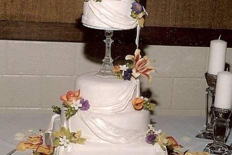 Stacked and separated round and square tiers are covered in fondant and adorned with beautiful drapes and real flowers.