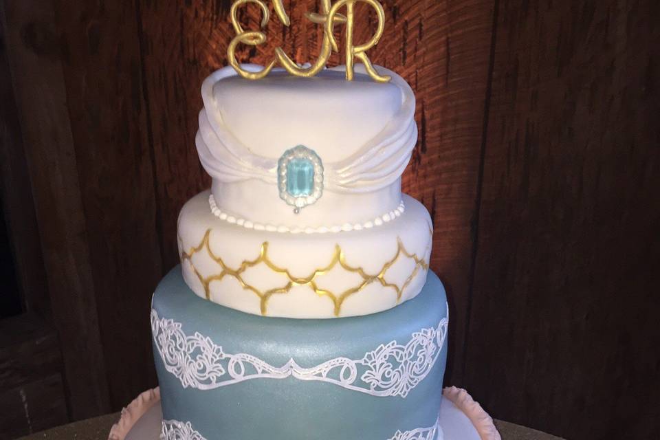 Fondant covered cake with: Ruffled rosettes of fondant, Isomalt jewel, flexible lace, and hand crafted monogram give this cake a bit of a shabby chic, but classic look.