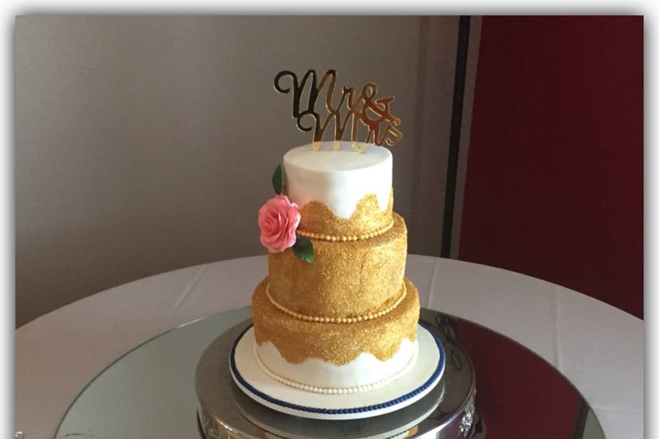 Golden sugar sparkles in a modern wave. Cake was lightly airbrushed with a golden pearl sheen. One giant hand-made coral rose.