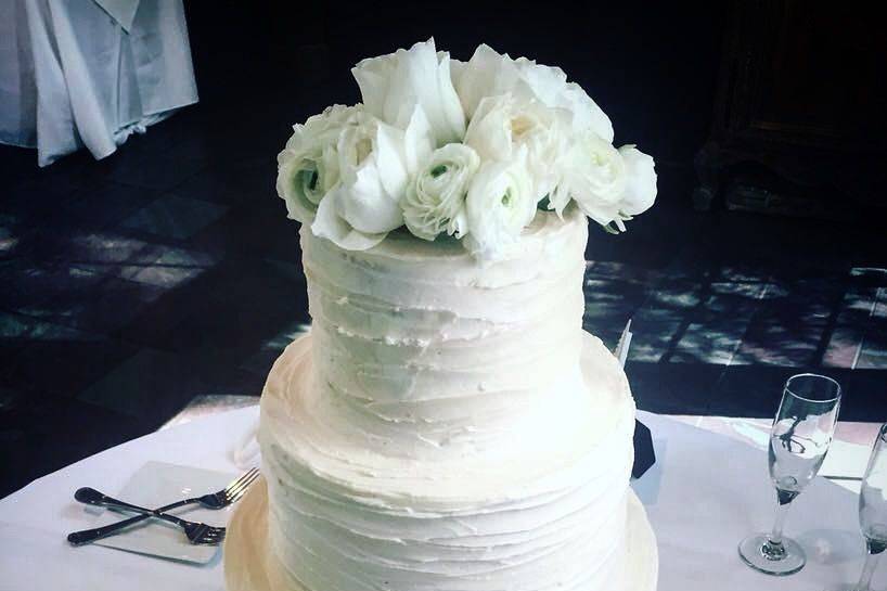 American Buttercream in an organic striped texture brings life to this vanilla and strawberry 4-tier bridal cake. We added natural ranúnculus to top off the cake and a leafy border with tiny blossoms at the base