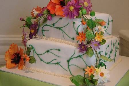 A delicate square vanilla cake covered in smooth white fondant and green buttercream vines. The cascading wild flowers are hand made and hand painted sugar flowers.