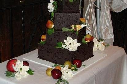 A decadent 4-tiered chocolate brownie groom's cake with chocolate buttercream and dark chocolate ganache. Decorated with hand made sugar magnolias and fresh fruit and herbs for the rehearsal dinner.