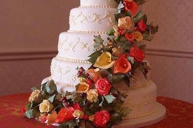 This amazing 5-tiered almond creme cake is covered in ivory fondant and embellished with pale yellow scrolls. An unbelievable assortment of hand sculpted sugar lilies, roses, leaves and berries cascade down the front. Perfect for a beautiful fall wedding.
