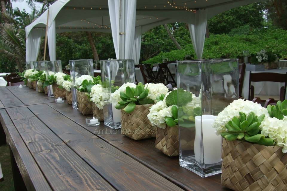 The long table is a current trend and this head table had repeating hydrangea and naupaka arrangements in lauhala baskets for a casual, beach themed looked.  Pillar candles in tall square vases added interest and light for the evening at this outdoor wedding.