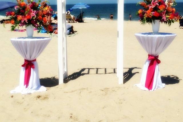 Beach Ceremony with 2 cocktail tables and white wedding arch