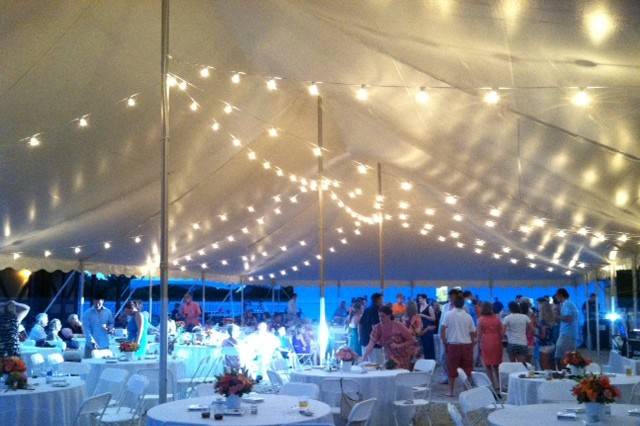 Tented wedding reception with draping California lighting, linen covered tables and white plastic folding chairs