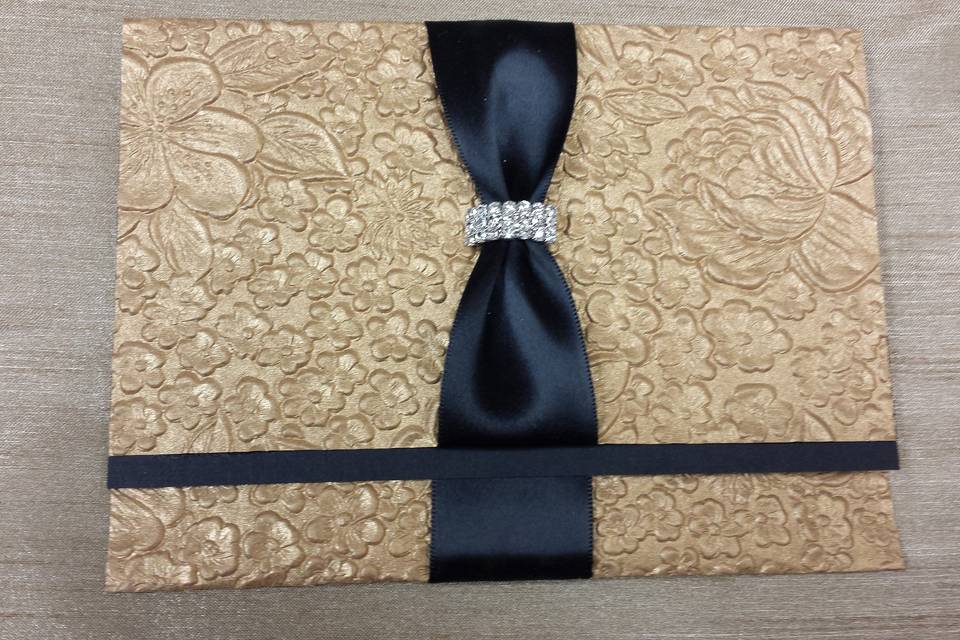 Gold embossed paper with a black linen strip in the center and black satin ribbon with curved buckle.