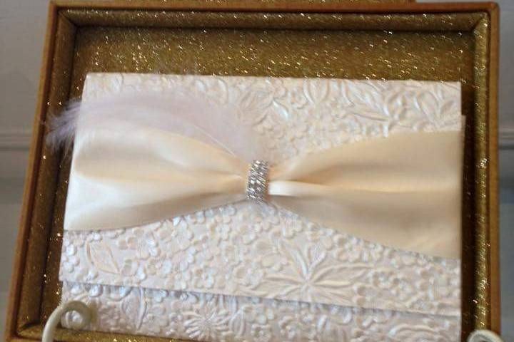 Tri-fold invite, in a gold glitter box, with an ivory satin ribbon and curved rhinestone buckle and a feather to top it off.