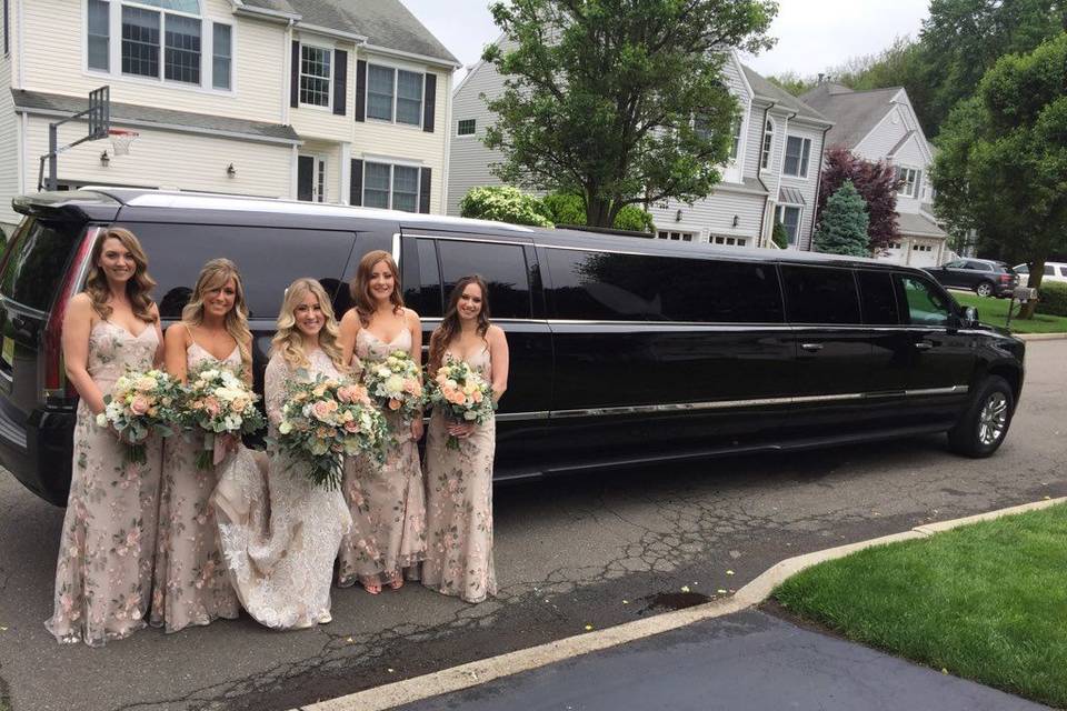 The perfect bridal party poses with our 12-passenger Cadillac Escalade.