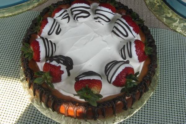 Cheesecake with chocolate drizzled down sides, chocolate-dipped strawberries.