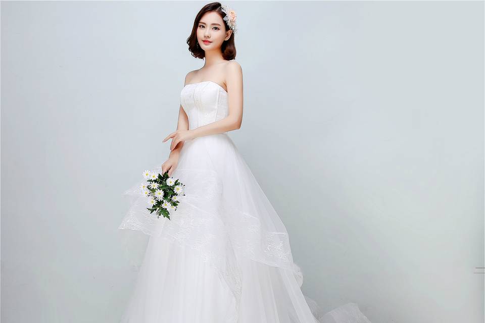 Classic strapless upper bodice covered by soft lace netting is seamlessly combined with irregular multi-layered voluminous skirt. The wholes dress offers a concise but iconic look for brides who prefer simple and streamlined design, and brings out the natural beauty of the woman within love.