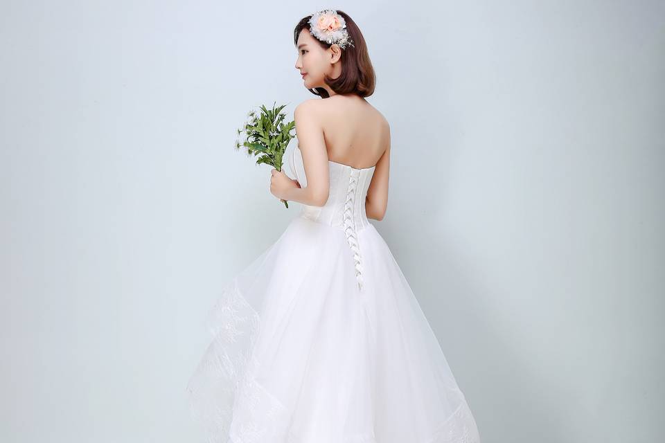 Classic strapless upper bodice covered by soft lace netting is seamlessly combined with irregular multi-layered voluminous skirt. The wholes dress offers a concise but iconic look for brides who prefer simple and streamlined design, and brings out the natural beauty of the woman within love.