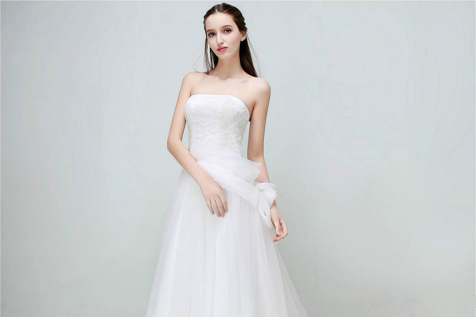 This A-line gown is featured with concise floral lace design, streamlined silhouettes and luxe fabrics. The wrinkled layers of soft organza is made into a ruffled ribbon extended from one side of waist to the other side hips. Moderate volume skirts create prosperous feeling to call the inner princess or fairy of the bride.