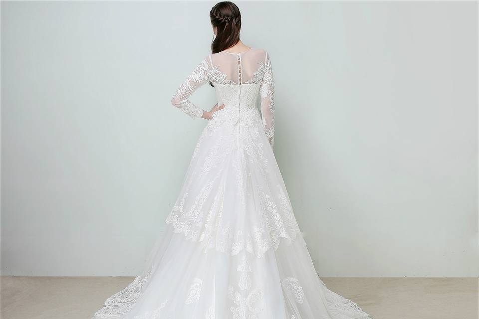 Fully-embroidered with elegant French lace appliques and hem lace beaded with iridescent sequins and pearls, this long-sleeve off-shoulder dress offers a touch of princess-like elegance and edginess. Its flutters of sheer fabric and flattering streamlined A-line silhouettes make the bride who owns it speak out their inner goddess or muse. The carefully arranged large lace paneling along the multi layered tulle train across the whole dress evokes the soul of effortless and flirty feminine glamor.