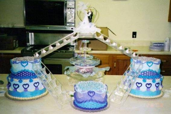 LOVE SUPREME:  2-tier plus 2-tier plus the anniversary cake connected with two sets of crystal stairs leading up to a balcony suspended over a sparkling fountain.  These cakes are decorated with shell hearts, candelabra swags, rosettes, basket weave, ribbon swags and cornelli lace.  Decoration of fountain may not match picture.