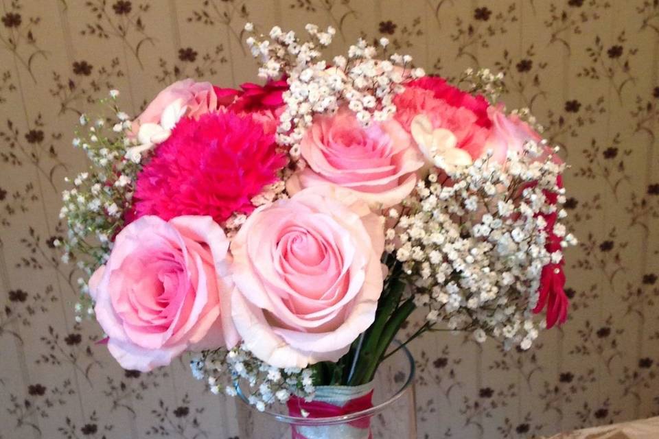 Shades of pink bridal bouquet using roses, carnations, and gypsophilia.  Ribbon is French braided on the stems.