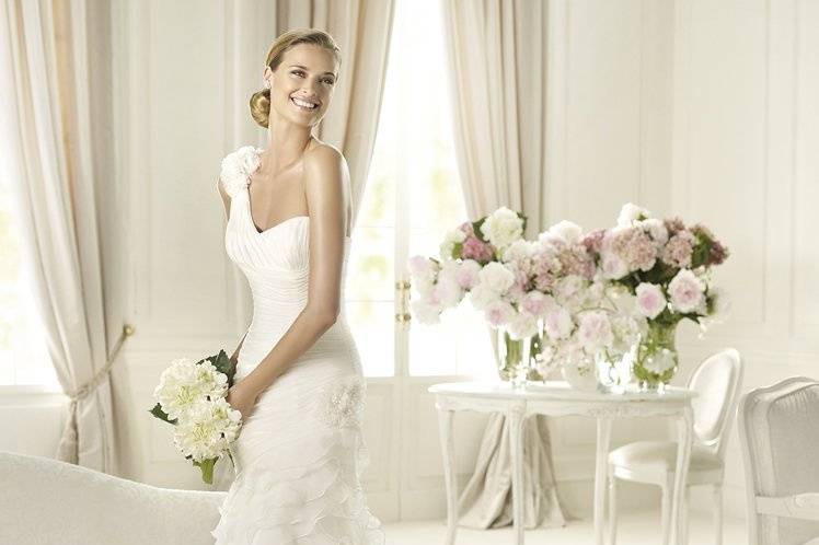 FAUNAFauna is a delicate silk garza wedding dress from the Dreams by Pronovias 2013 collection. It has a flattering asymmetric neckline and is decorated with silk garza flower appliqués on the shoulders and at the hip. The mermaid shape of this gown has a modern air and showcases its elegant frilled skirt and half train.