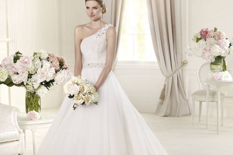 URIBEThe off-the-shoulder neckline is the most outstanding feature of this wedding dress. Uribe is a princess wedding dress from the Glamour by Pronovias 2013 collection. It features beautiful draping in tulle and original floral embroidery. Embroidery covers the bodice from shoulder to waist. The dress laces up at the back. The skirt has numerous layers of tulle and gives this model a romantic air.