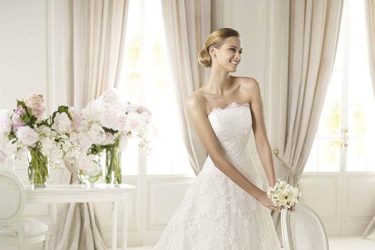 BERLINThe Berlin wedding dress by Pronovias 2013 expresses all the romance of a unique day.  Completely covered with lace, this tulle wedding dress is cinched in at the waist by a beautiful belt with a gemstone embroidery brooch that joins at the back with a stunning bow. A classic skirt, decorated with beautiful lace shapes, flows out below the belt and culminates in soft waves of lace all around the train. A subtle, sheer lace border highlights the strapless neckline.