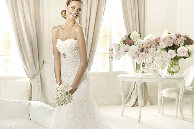 BERTABerta by Pronovias 2013 has a modern air that shines through in the cut. This tulle wedding dress has a sweetheart neckline with delicate edging and two bands that meet at the front, framing the wonderful lace on the bust.  The bands start at the sides, meeting at the front with a beautiful gemstone appliqué. The entire bodice is decorated with lace, which also adorns the hem of the dress. This model is ideal for brides who want to slim their figures and subtly highlight their curves.