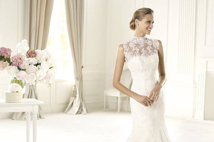 UGAZThe elegant Ugaz model from the Costura by Pronovias 2013 is made of delicate rebrodé lace and has a lovely off-the-shoulder neckline. It features a lace-up back. The waist is of this wedding dress is encircled by a grosgrain belt decorated with delicate beaded embroidery with a wonderful bow at the back. The skirt, decorated with delicate lace appliqués is even more elegant thanks to its scalloped hemline. This A-line design has an original tulle cape with beautiful lace embellishments.