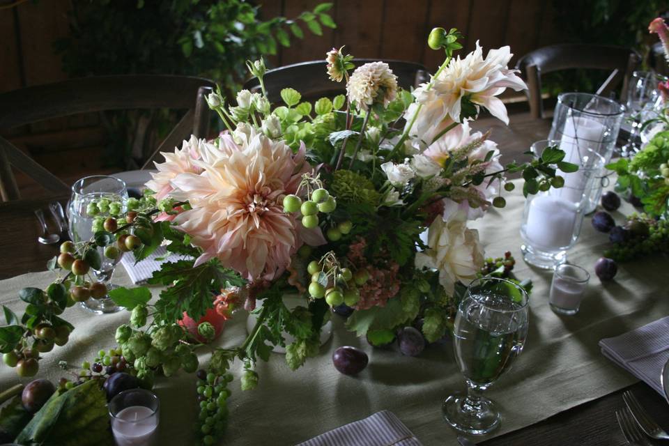 A centerpiece at an elegant barn wedding loaded with dahlias, grapes, crab apples and so much more by White Magnolia Designs.