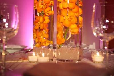 Clean cylinder vases filled with mango mokara orchids, clear crushed glass in base, topped with a floating votive.
