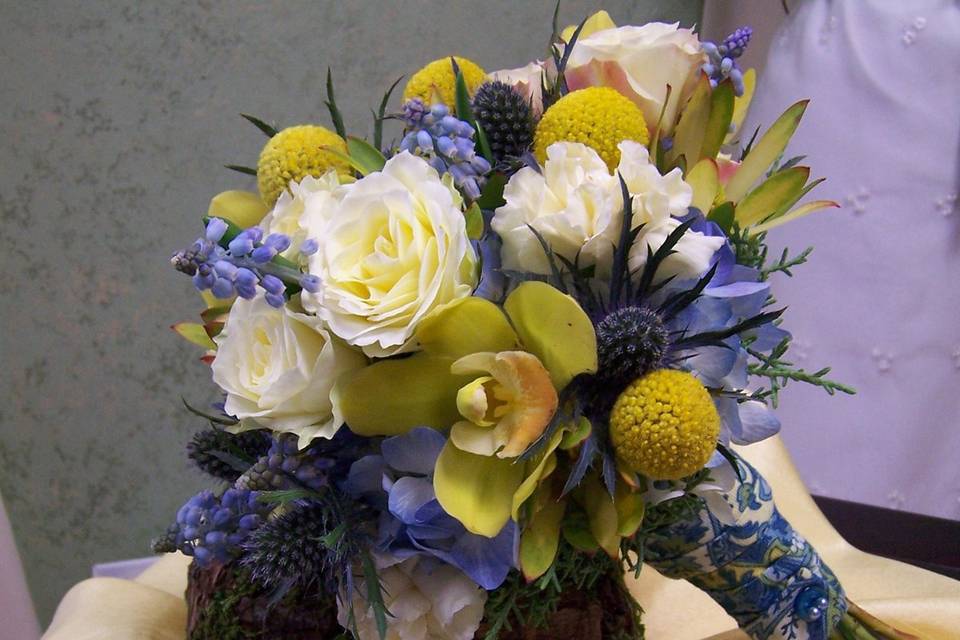 A rustic, yet elegant bouquet featuring roses, orchids, delphinium, blue thistle, and crespedia.