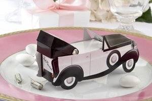 Before you drive away on that momentous day, drive them wild with style and something sweet!
Artistic flair and attention to detail has led to a wedding favor your guests will talk about at least as until the end of your honeymoon?and probably longer! Reminiscent of a vintage make and model, the Getaway Car Favor Box is a spectacular way to transport sweet treats to your reception tables.
The aristocratic car, sleek and sophisticated in dramatic black with pink and white accents, features a pink heart as a hood ornament. The expandable, black roof is equally as charming as the two tin cans flying from the back of the car, tied right below the 
