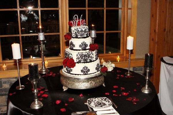 Black and white damask wedding cake on black satin table linen surrounded by a variety of pillar candles.