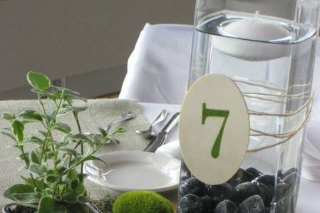 Detail of guest table centerpiece on tree round with river rocks, mosses and succulent plant.