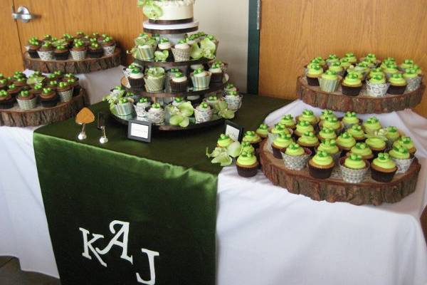 Wedding cake/cupcake display featuring handmade runner with handpainted monogram. Cupcakes sit on tree rounds and mimick wedding colors and berries in bride's bouquet.