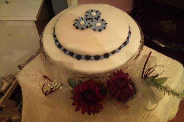 This is a Vanilla, Butter, Nut cake, iced with complimentary icing, then covered with fondant.  The cake is decorated with handmade Black & Purple Daisys finished with white sparkly centers, then bordered with a Ball Border in the same colors.