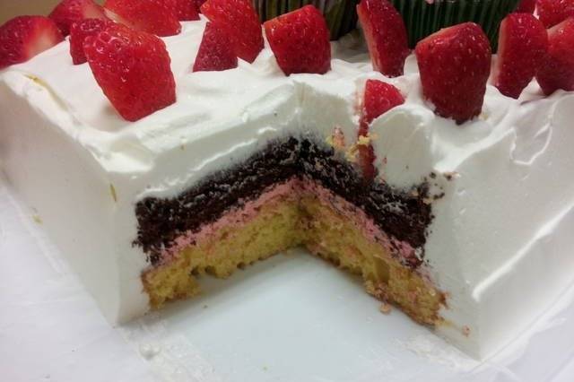 View of Strawberry Shortcake with Strawberry Creme filled once cut. The top layer is a Chocolate Butter cake, then the Strawberry Creme layer.  The top layer of cake is Yellow Butter. The entire cake is surrounded by whipped cream, then decorated.