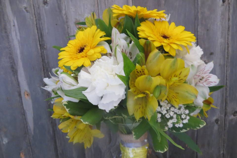 Fun, country bouquet with yellow and white alstromeria lilies, yellow gerberas, white carnations and a touch of million star babie's breath with a burlap/grey/yellow wrap.