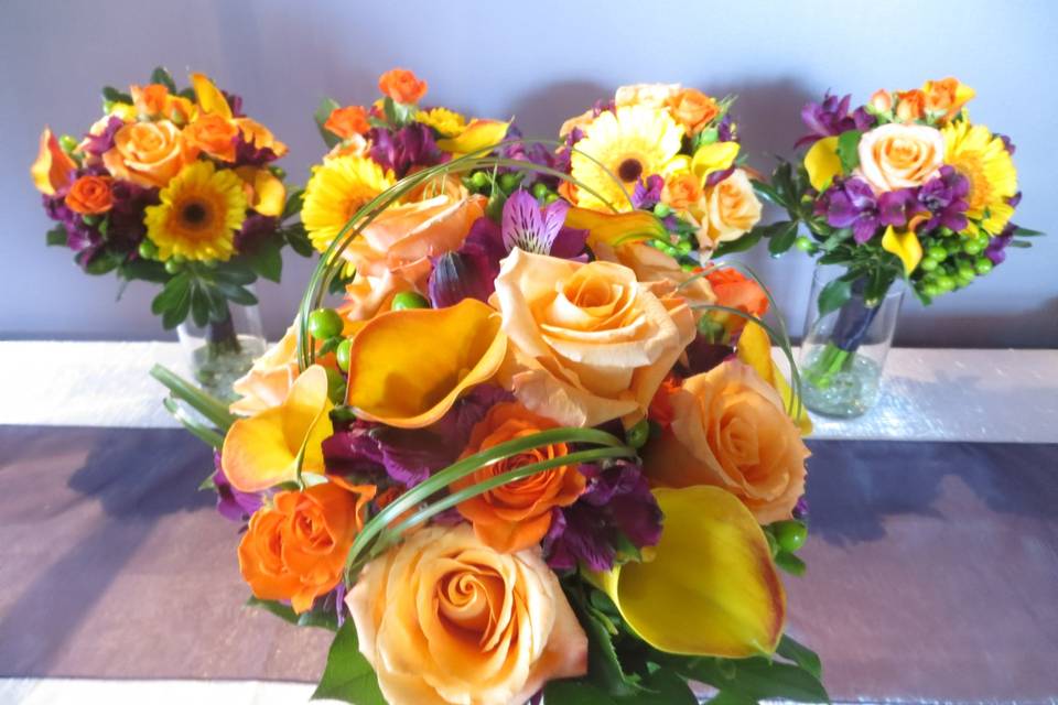 Bridal bouquet and four bridesmaids bouquets to compliment. Bridal bouquet features stunning flame calla lilies, orange unique roses, orange spray roses, purple alstromeria lilies, green hypericum berries and salal and bear grass accent. Gorgeous! Bridesmaids very similar but with gerbera daisies added.