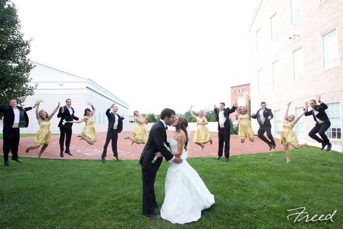 Newlyweds kissing with guests jumping in the background