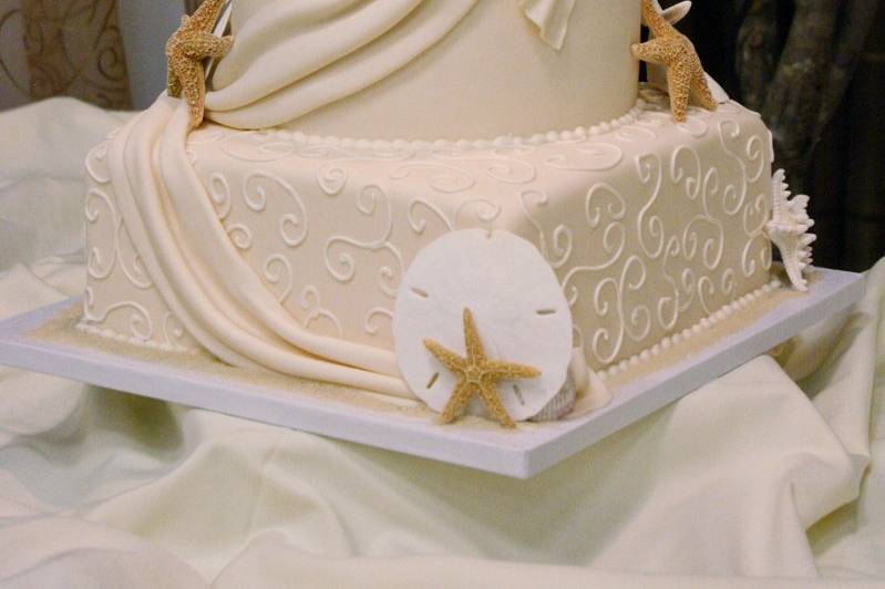 Elegant, ivory seashell wedding cake with real shells, fondant drapes, and hand-piped buttercream scrolls.