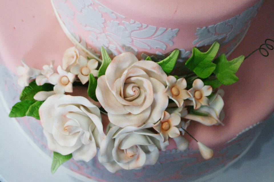 Gorgeous wedding cake covered in light pink fondant and adorned with gray damask stenciling.  Floral piece on the front was hand-made from edible materials.