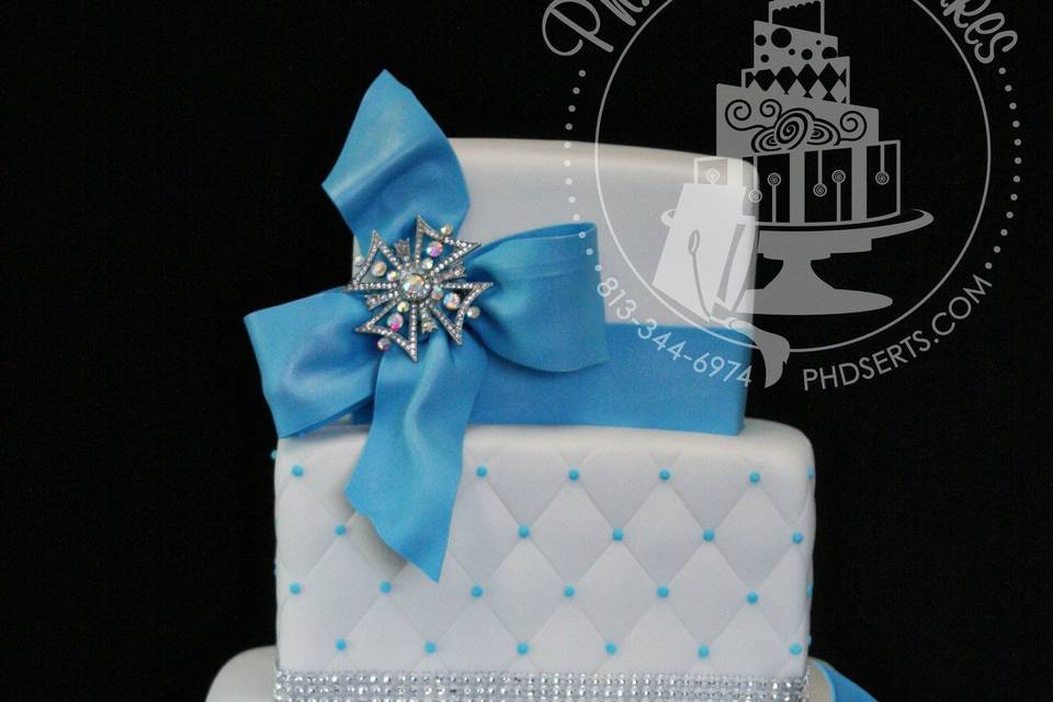 Fondant-covered square wedding cake with blue Damask, quilting, and large romantic blue bows.  Silver brooches and faux diamond ribbons added just enough sparkle to this beauty!